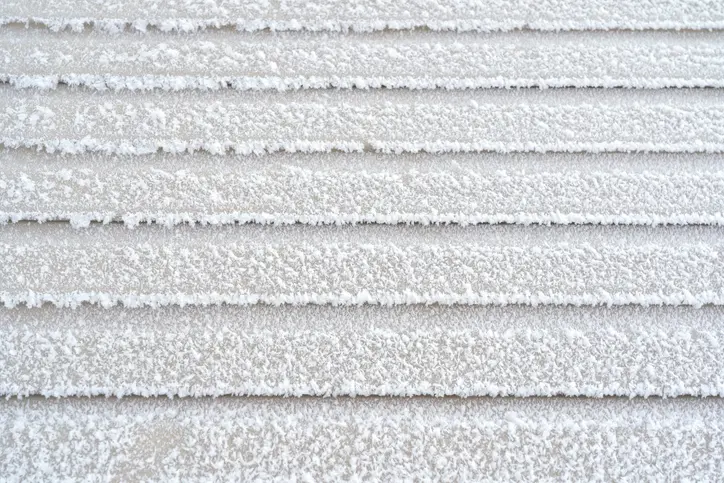 The wall of the building is covered with beige plastic clapboard. There is white fluffy frost on the surface of the siding. Background. Texture.