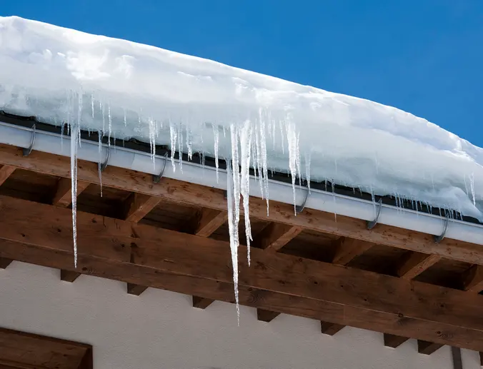 Long icicles and snow overhaning the roof and gutter of a building.