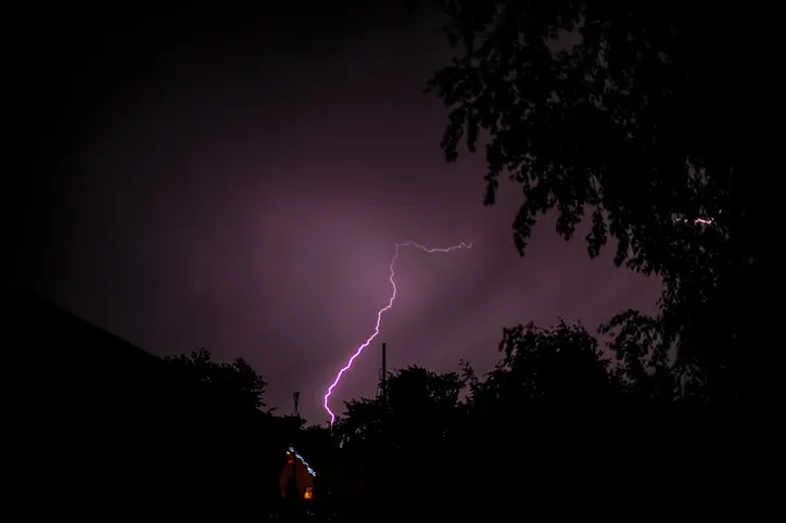 A lightning strike at night with trees in the foreground