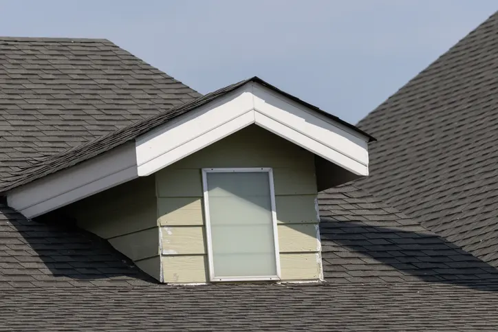 A roof with a window in the middle of it. The window is covered by a white frame